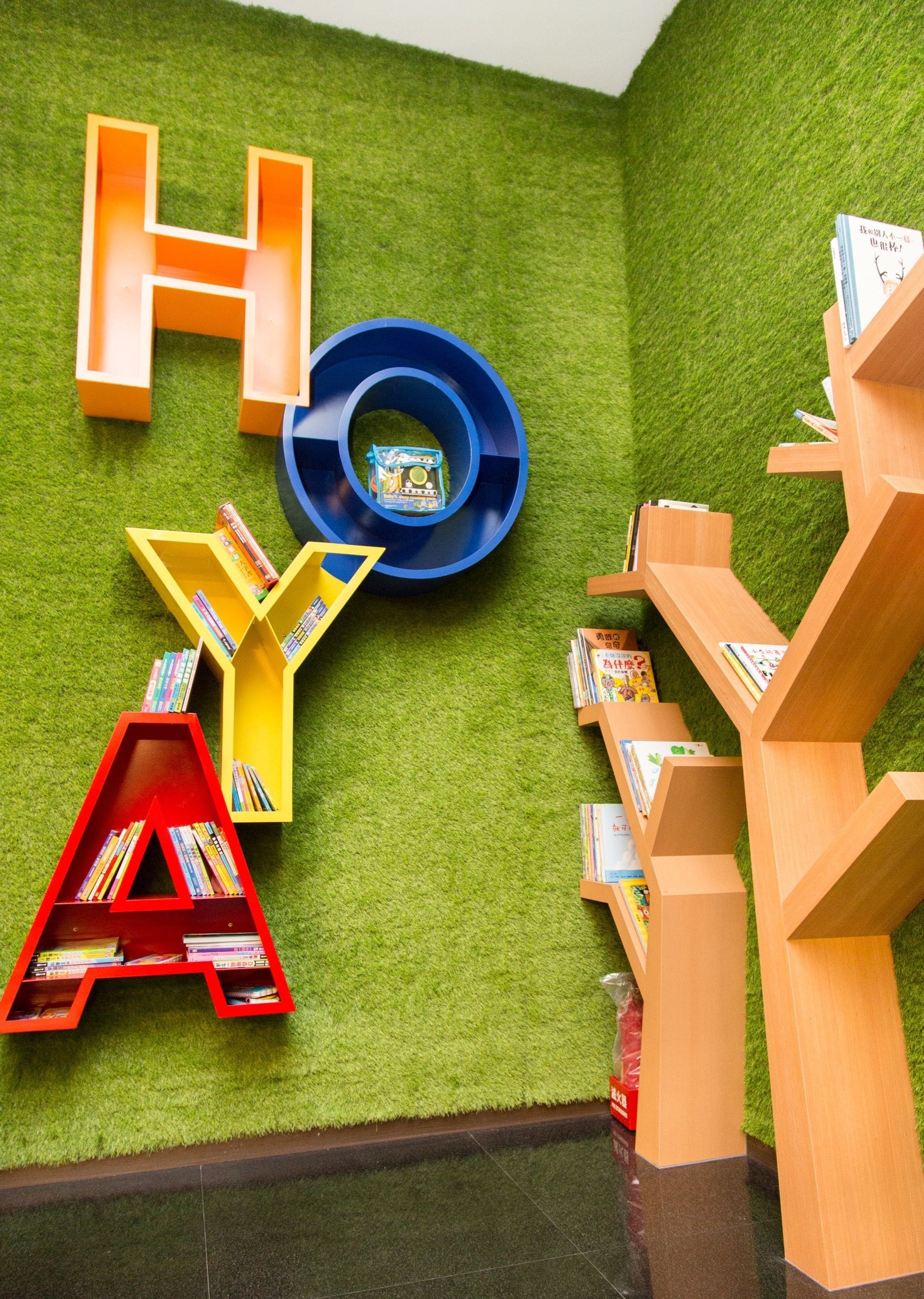 Una biblioteca infantil con estanterías con forma de letras y un expositor circular central.