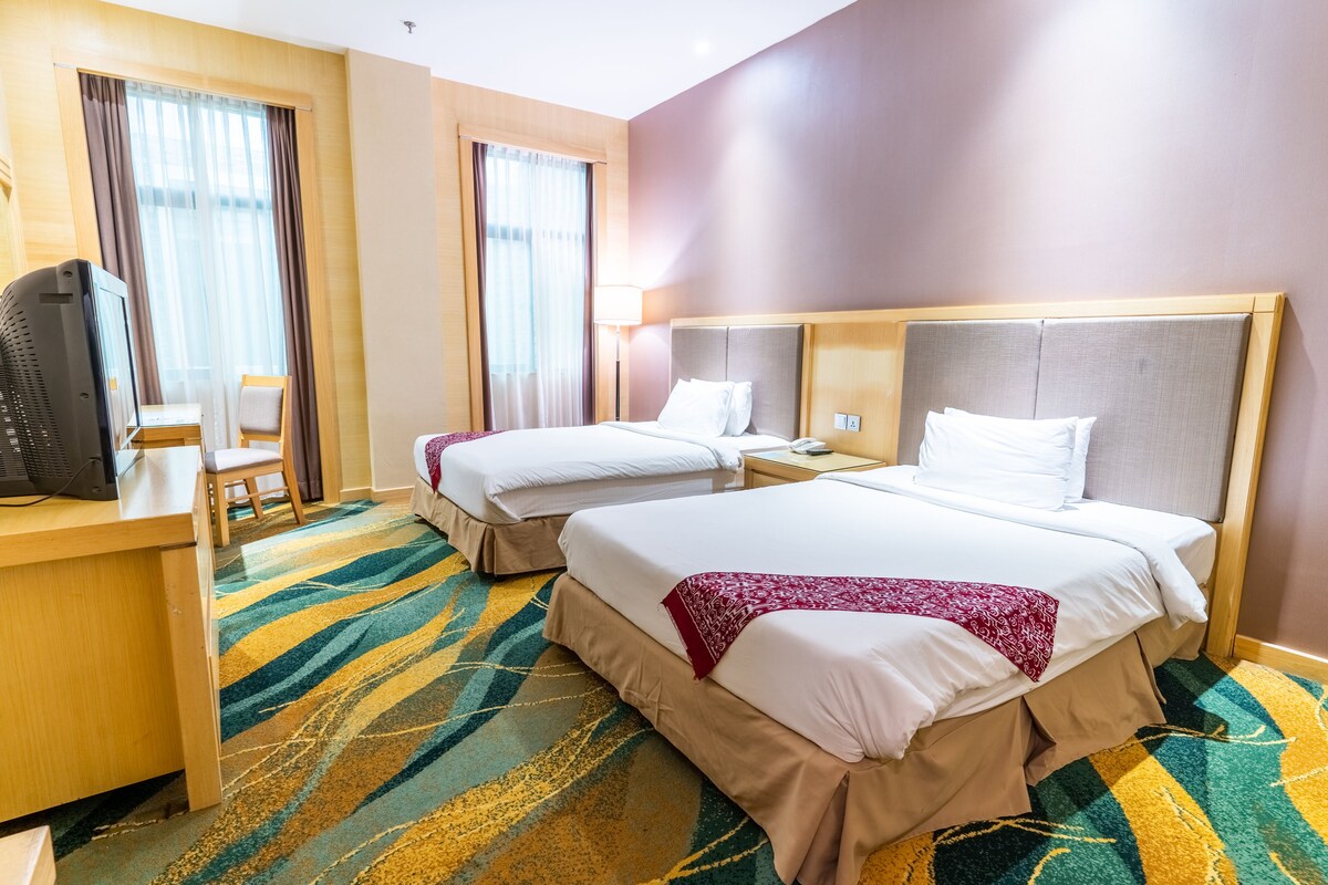 A hotel room with two beds, a desk with a computer, and a chair.