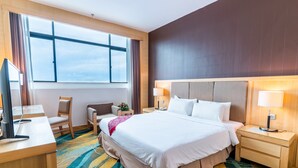 A hotel room with a large bed, two bedside tables with lamps, a desk with a computer, a chair, and a large window with curtains. - Imperial Palace Hotel (Miri)