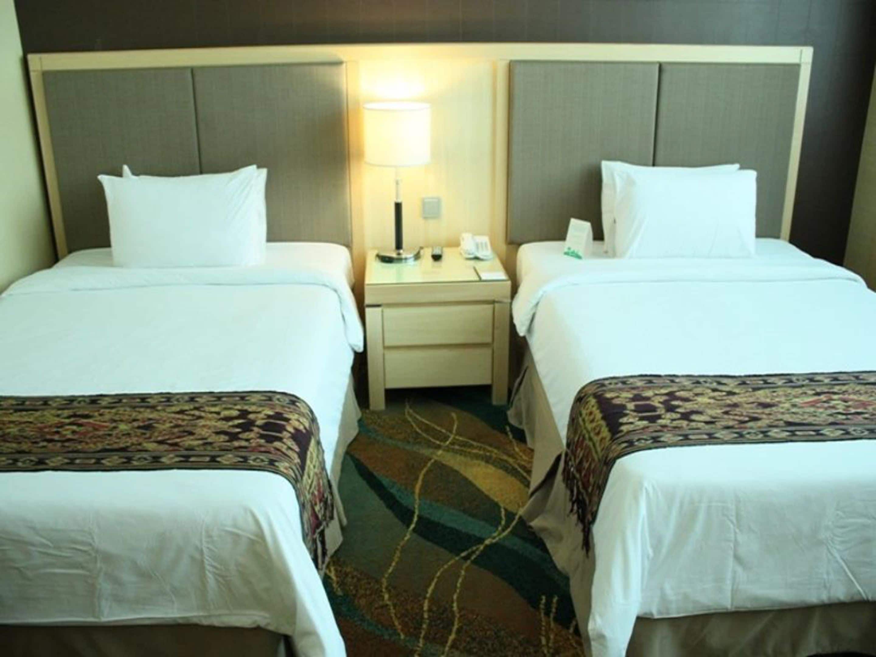 A hotel room with two single beds, a nightstand with a lamp, and a telephone.