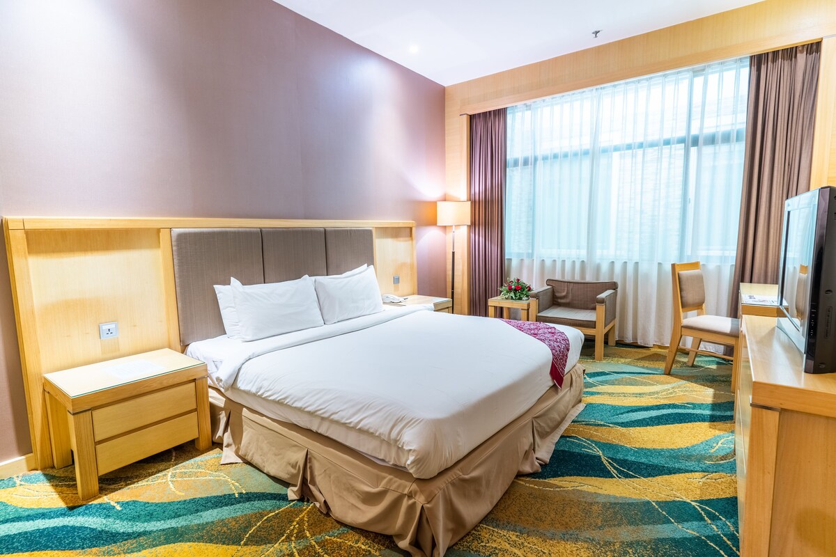 A hotel room with a large bed, a desk with a television, a chair, and a nightstand.