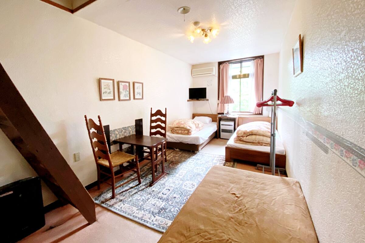Una habitación pequeña con cama, escritorio, silla, televisión y ventana con cortinas.