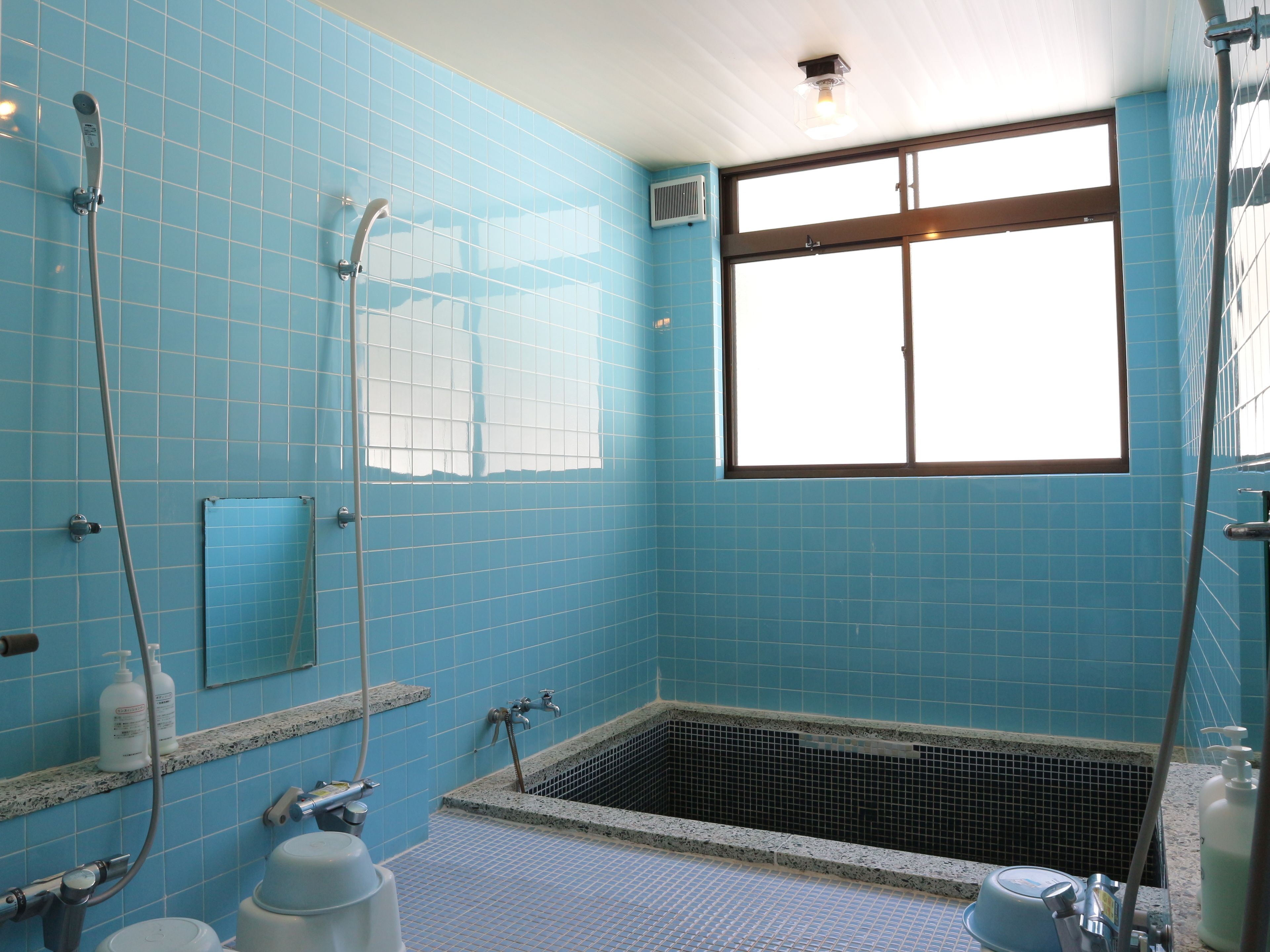 A bathroom with blue tiled walls, a window, a bathtub, and a shower.