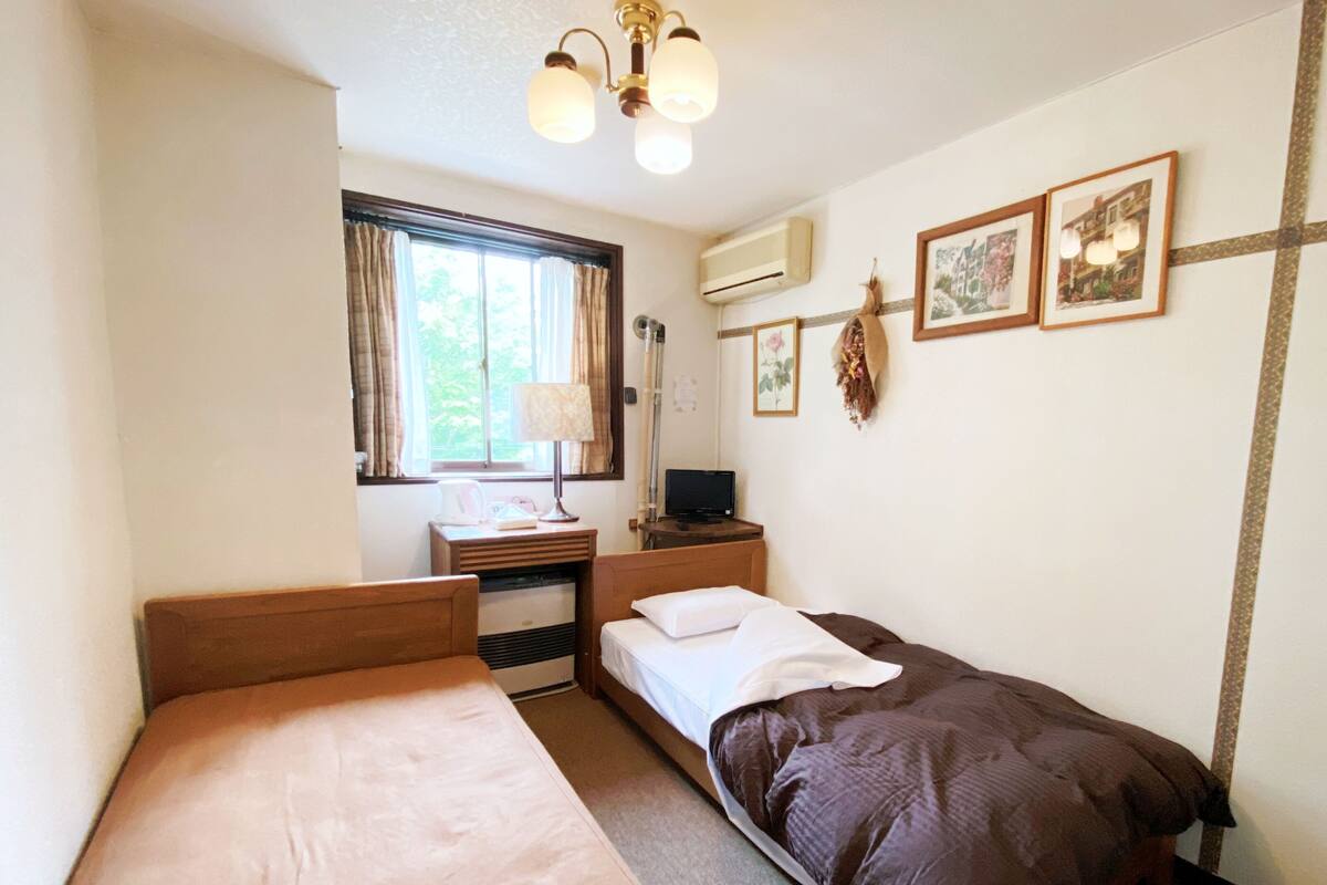 Un dormitorio con dos camas, un escritorio, una lámpara y cuadros en la pared.