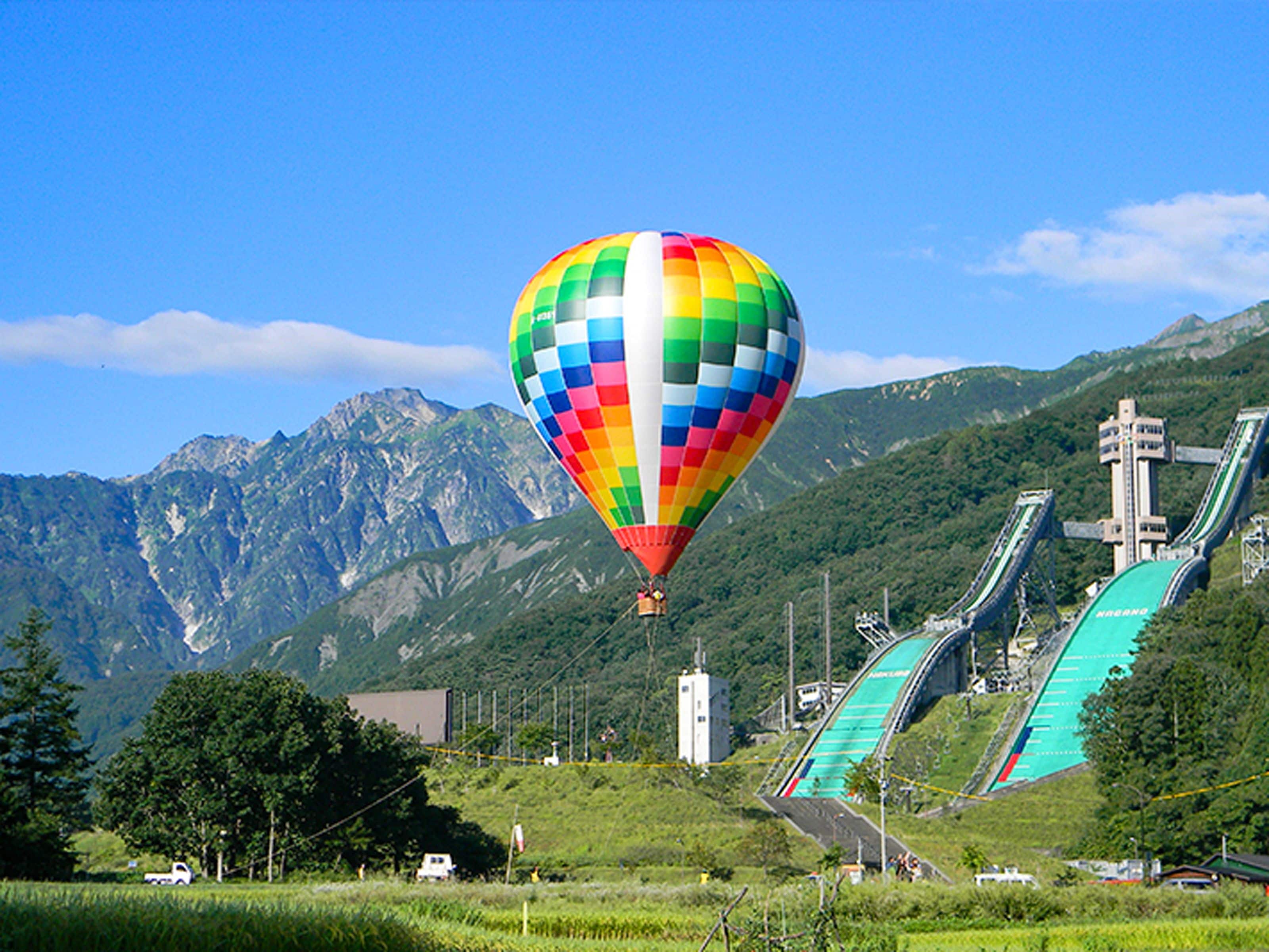 Un globo aerostático colorido sobre un paisaje montañoso con un telesilla al fondo.