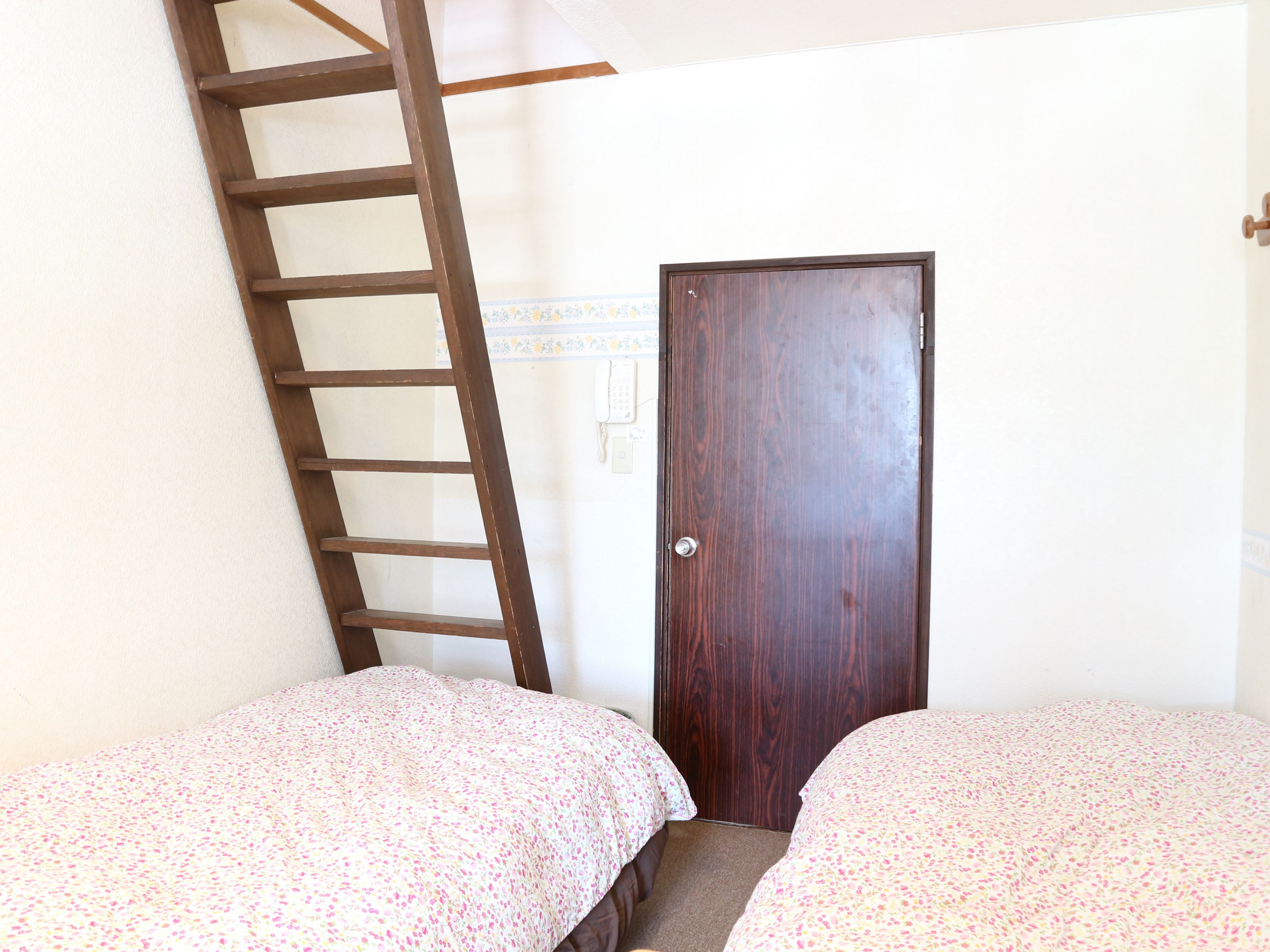 A room with two beds, a wooden ladder, and a door.