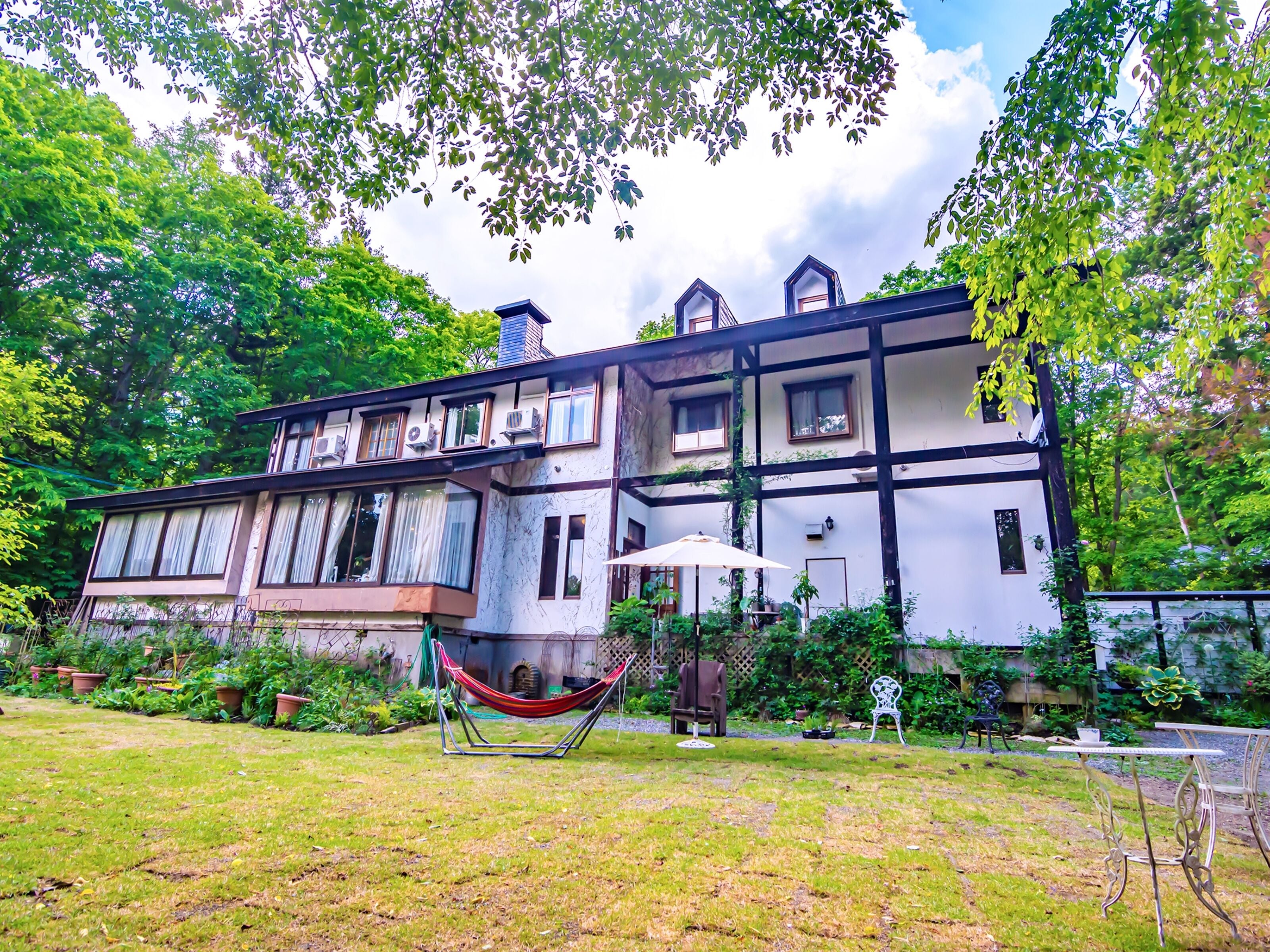 A two-story house with a garden, a hammock, and outdoor furniture.