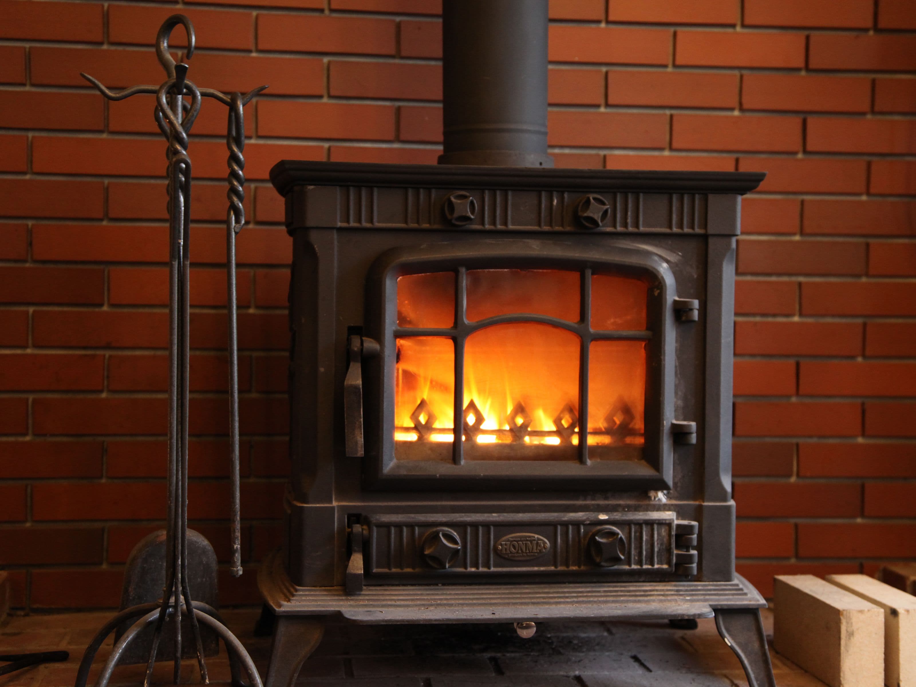 A wood-burning stove with a brick wall background.