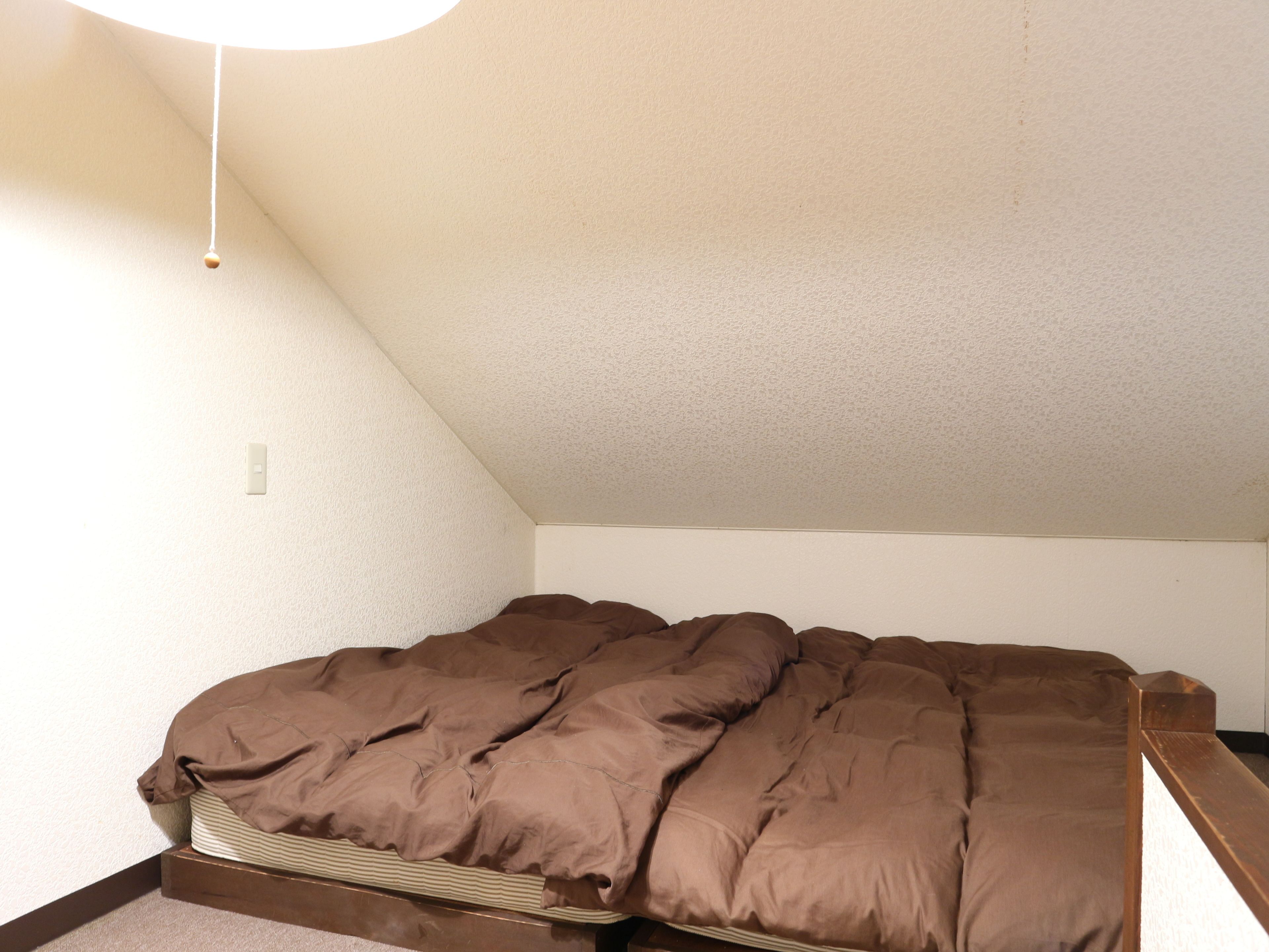 A single bed in a room with a sloped ceiling and a light fixture.
