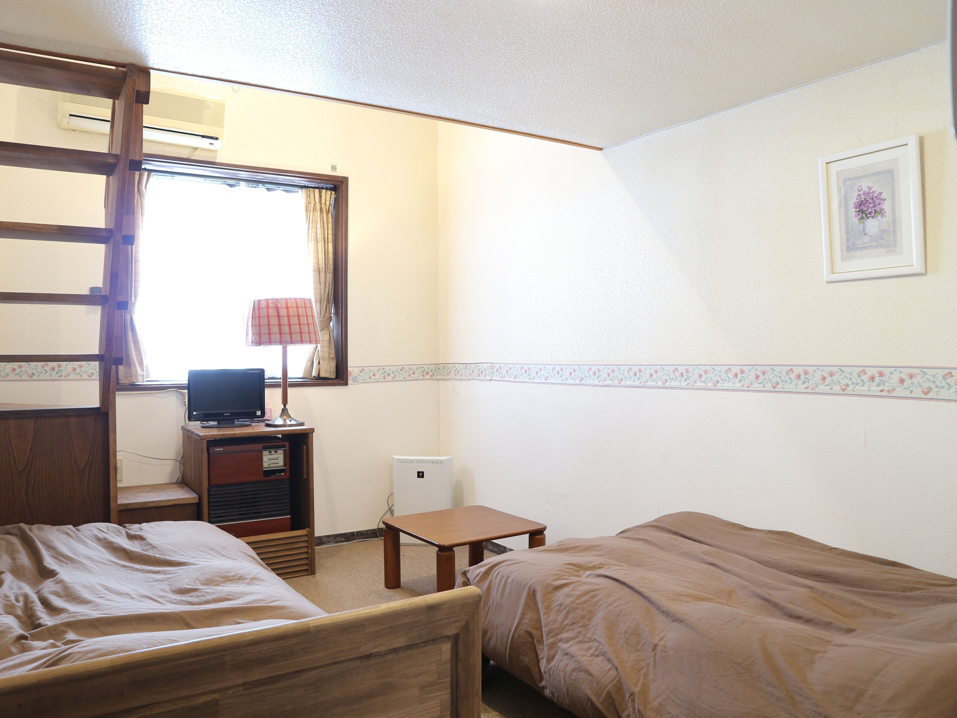 Une chambre avec deux lits, un bureau avec un ordinateur, une lampe et une fenêtre avec des rideaux.