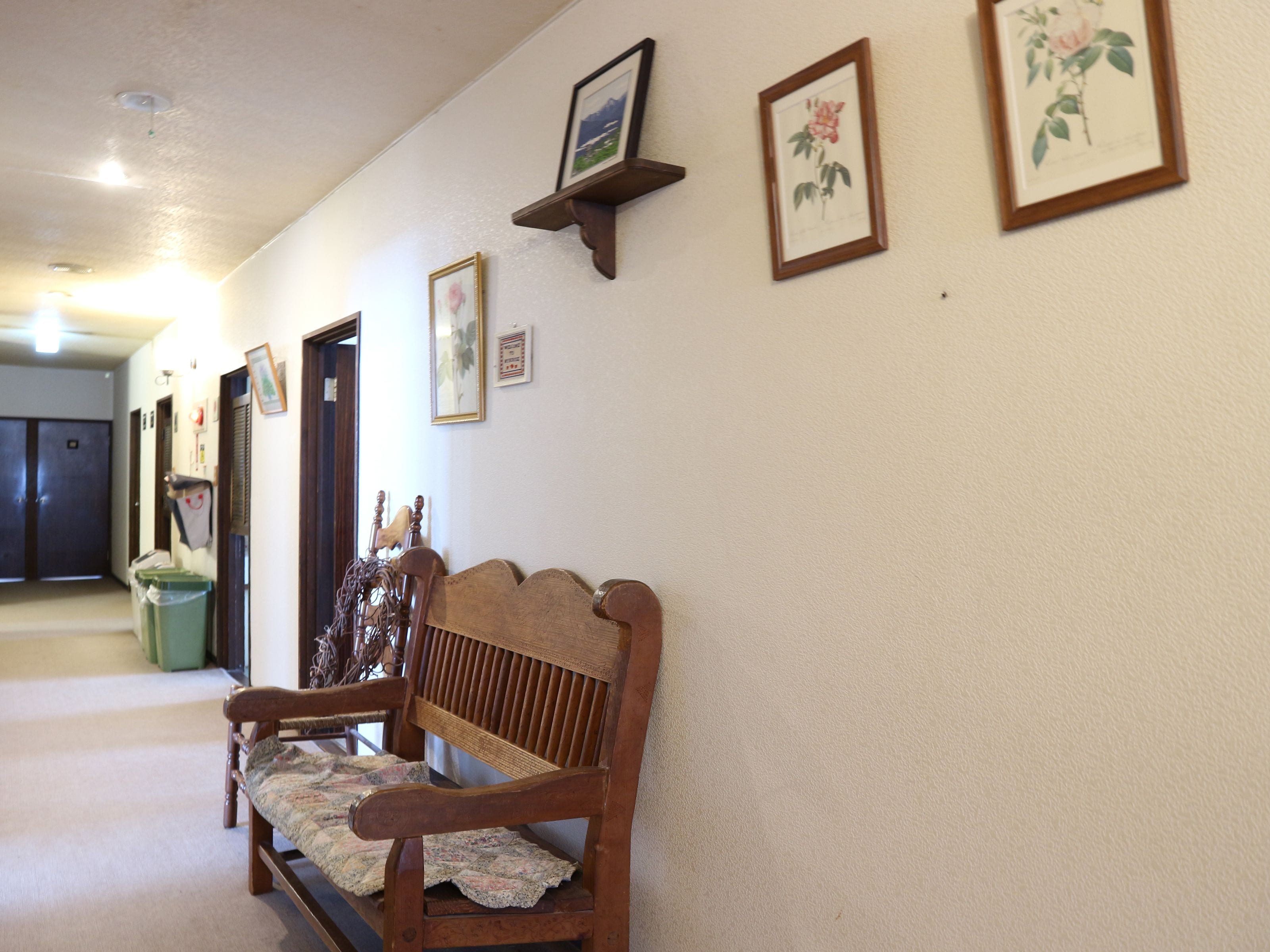 A hallway with a wooden bench, framed floral artwork on the walls, and a door at the end.