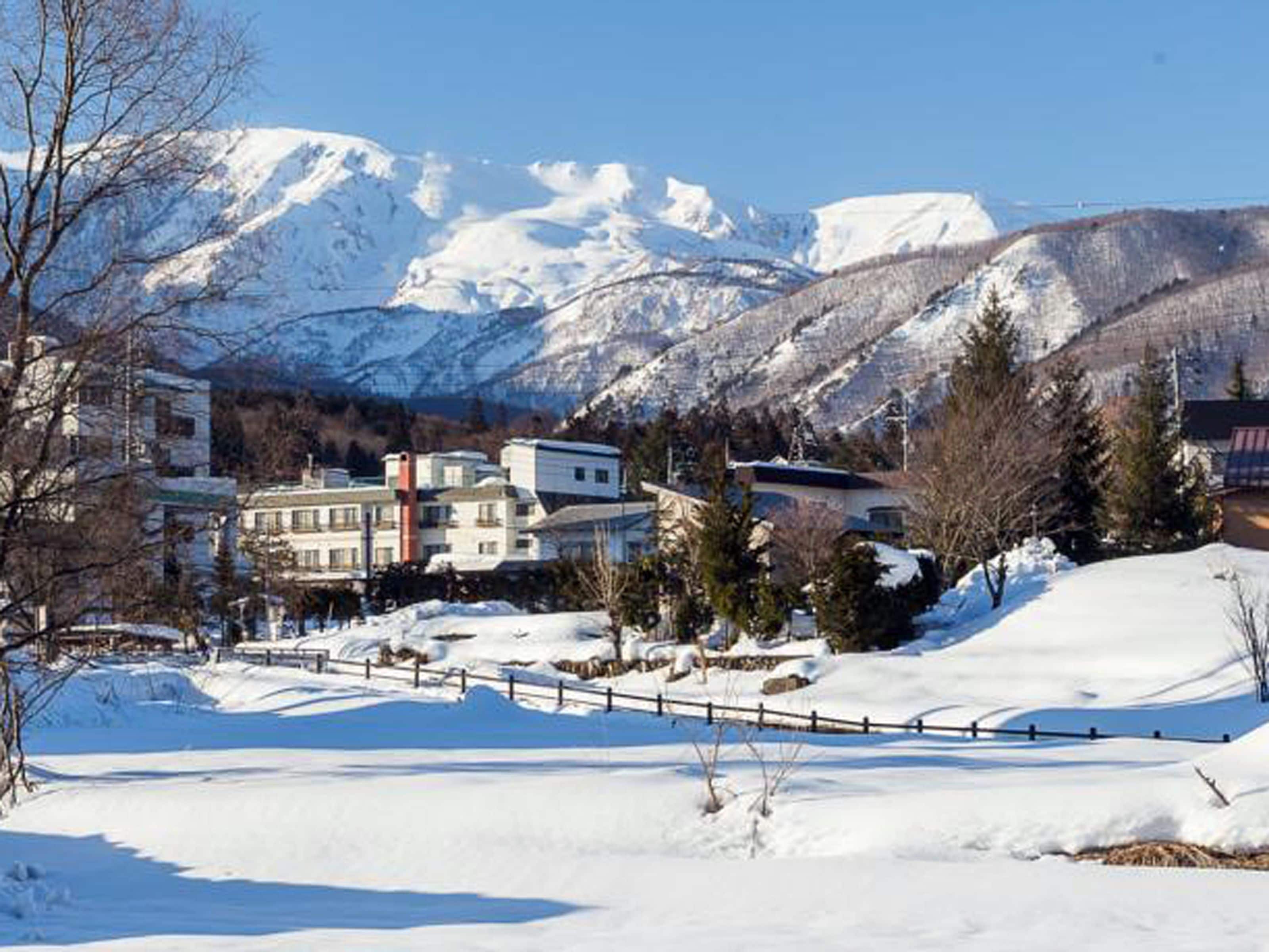 A snow-covered landscape with a building complex in the foreground and mountains in the background.