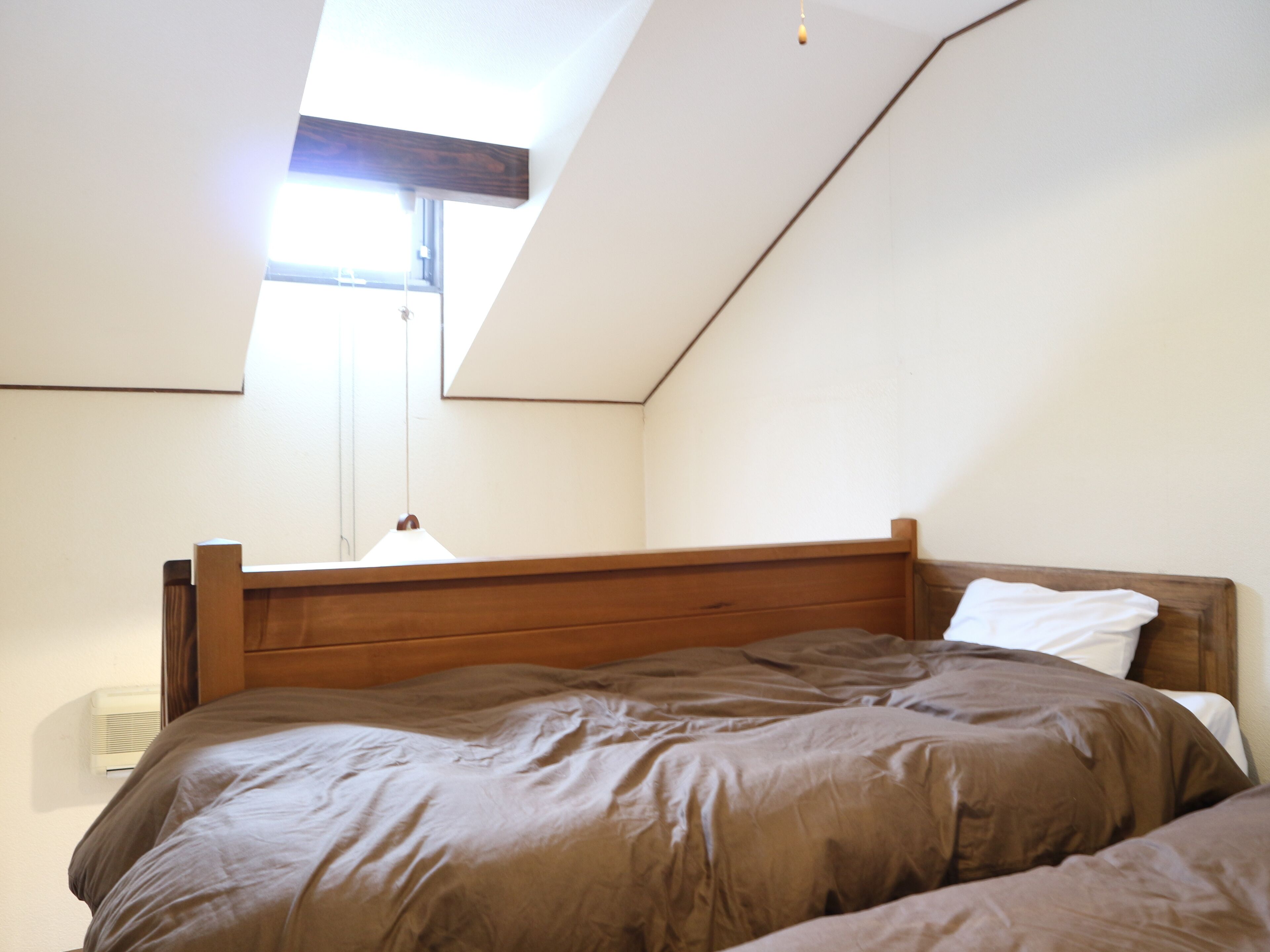Camera da letto con soffitto spiovente, testiera in legno e finestra che lascia entrare luce naturale.
