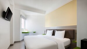 Una habitación de hotel moderna con una cama grande, un televisor de pantalla plana montado en la pared, un escritorio pequeño con una silla y una ventana que deja entrar luz natural.