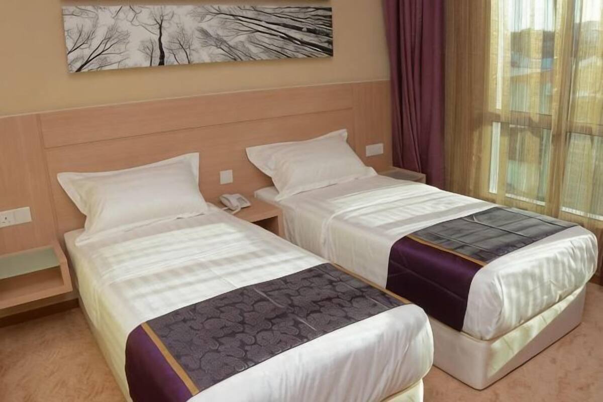 A hotel room with two single beds, a nightstand with a phone, a painting on the wall, and a window with curtains.