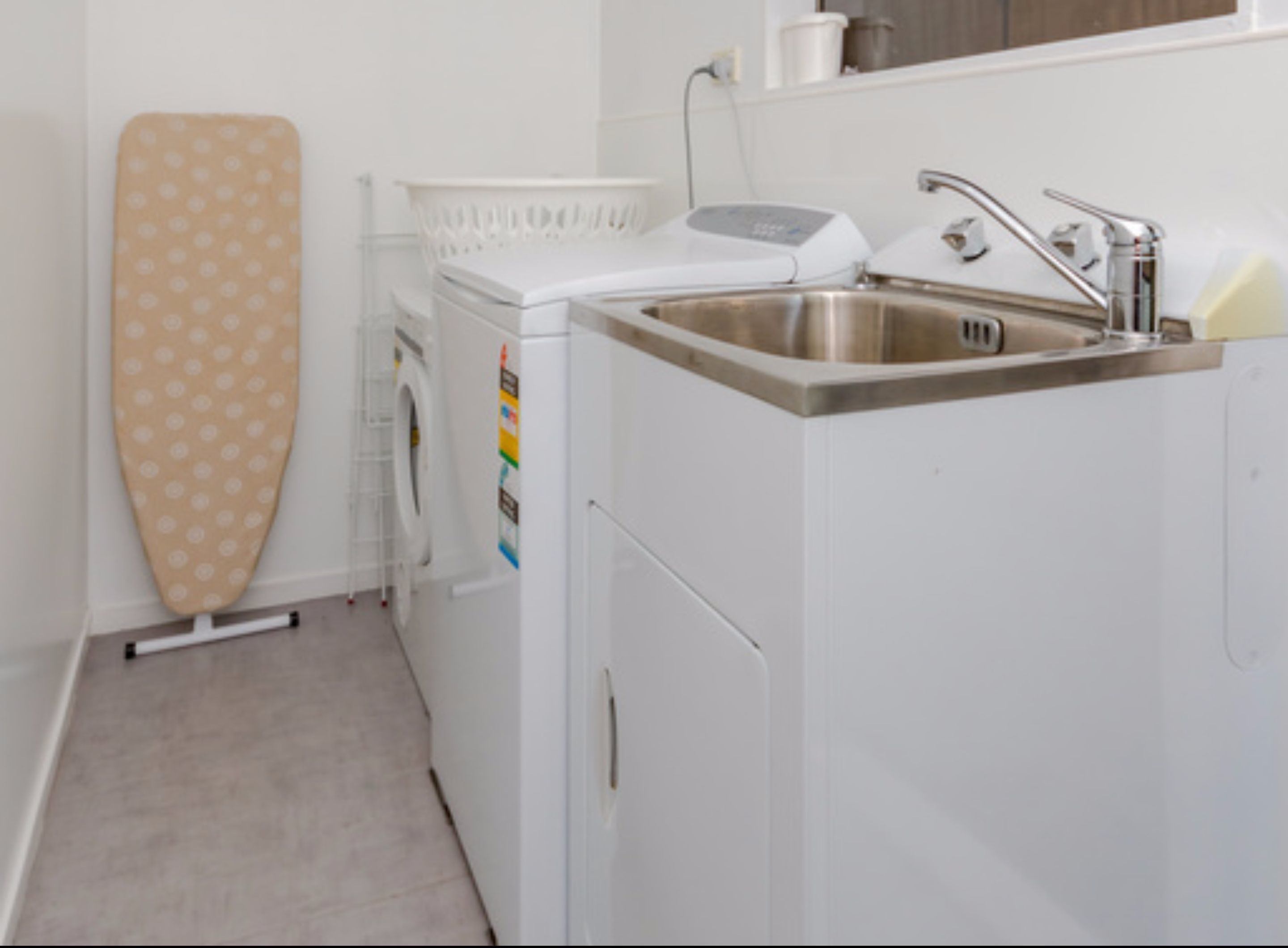 A compact laundry area with a washing machine, a drying rack, and a sink.
