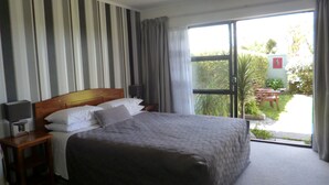 A hotel room with a large bed, a nightstand, a lamp, and a view of the garden through a sliding glass door. - Opua Boutique Seaview Motel (Opua)