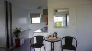 A compact living space with a kitchenette, two chairs, a small table, and a potted plant. - Opua Boutique Seaview Motel (Opua)