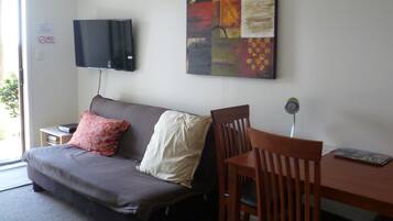 A room with a sofa, a TV mounted on the wall, a painting, a dining table with chairs, and a sign indicating no smoking.
