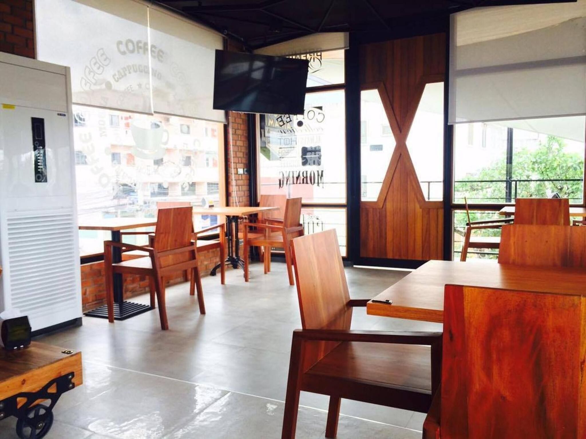 A cafe with wooden furniture, a TV screen, and large windows.