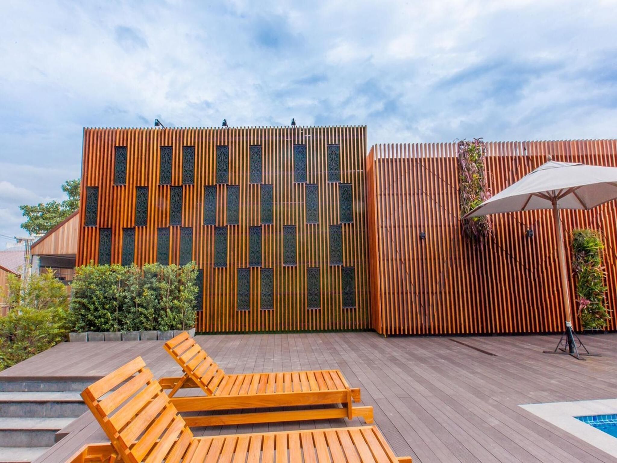A modern outdoor area with wooden deck, lounge chairs, and a pool.