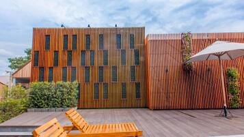 Un área exterior moderna con terraza de madera, sillones de descanso y piscina.