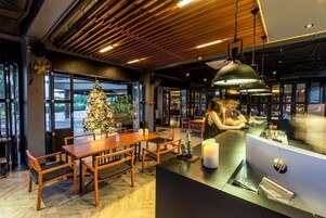 Interior de un restaurante con mesas y sillas de madera, un árbol de Navidad y una barra con un monitor de computadora.