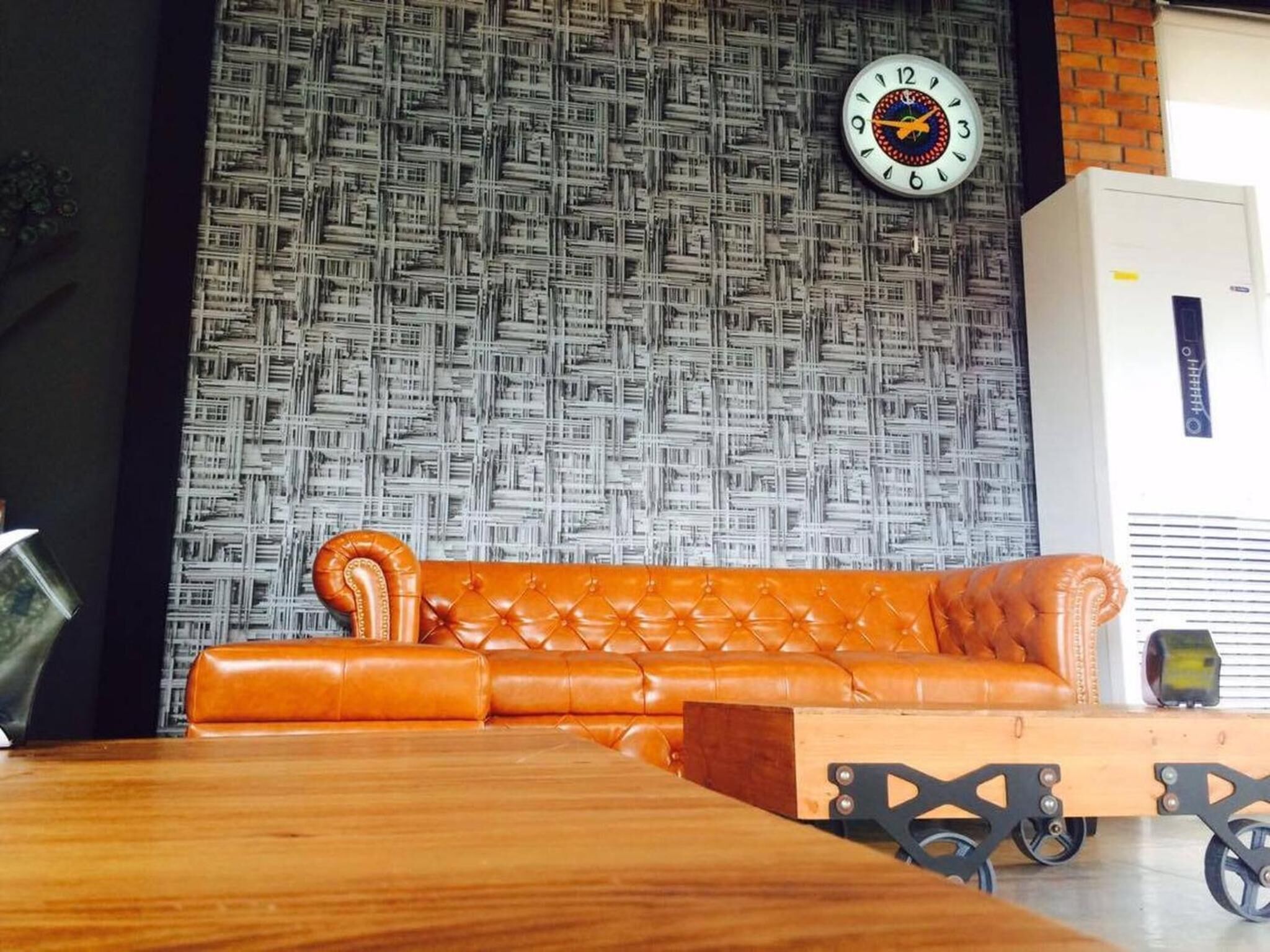 Una habitación con un papel tapiz estampado, un sofá de cuero marrón, una mesa de madera y un reloj en la pared.