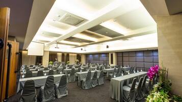 A conference room with multiple tables and chairs, equipped with water bottles and microphones, and a large screen at the front.