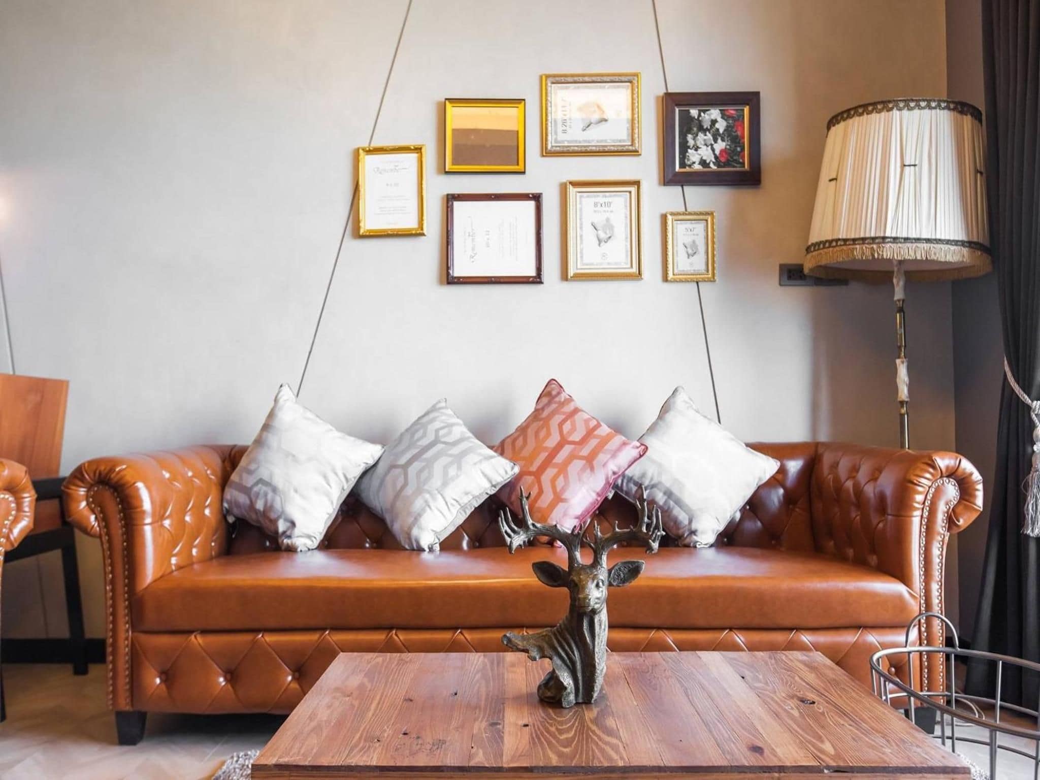 A brown leather sofa with patterned cushions, a wooden coffee table with a deer sculpture, and framed certificates on the wall.