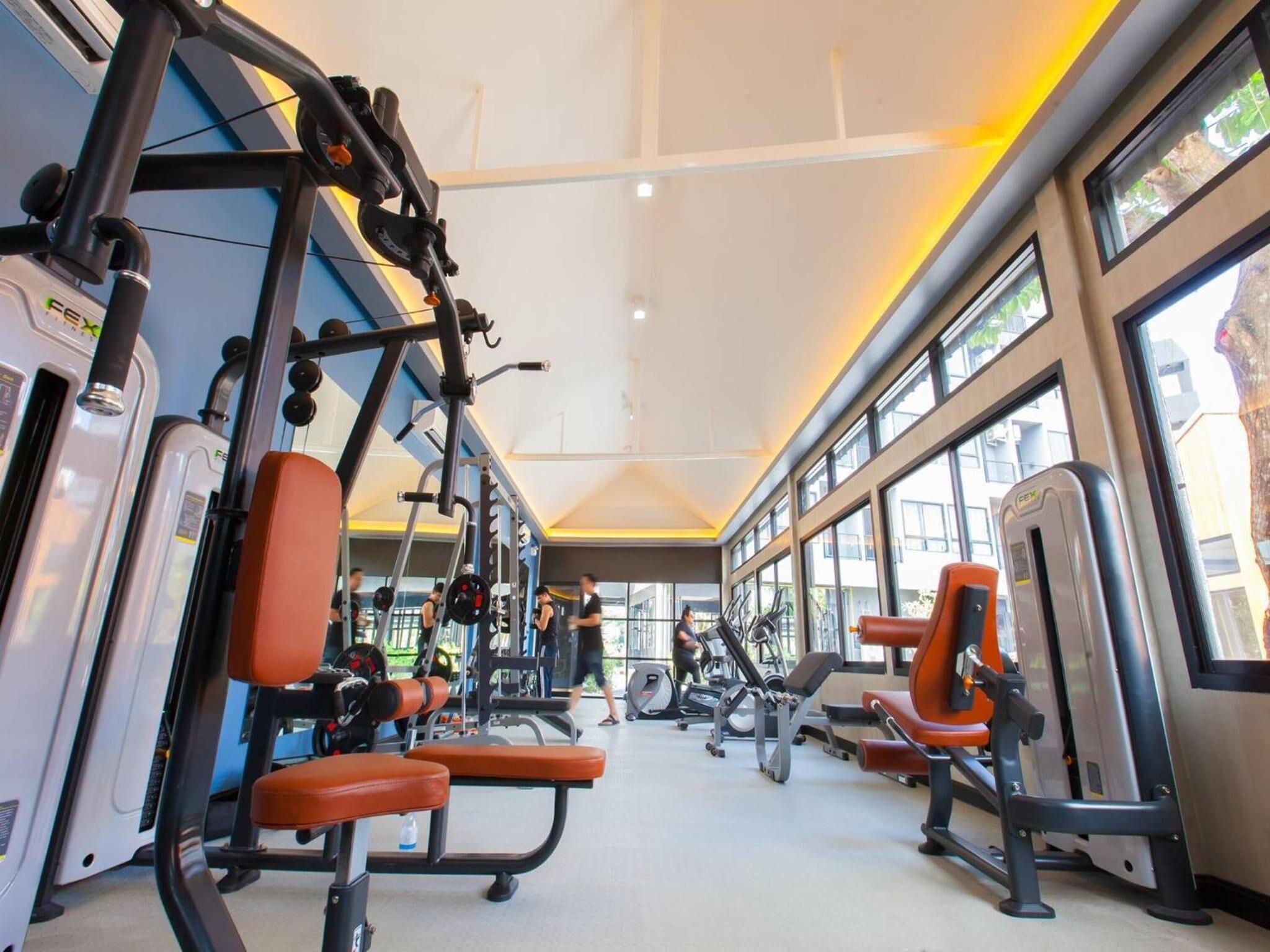 Un gimnasio con diverso equipo de ejercicio, ventanas amplias y techo alto.