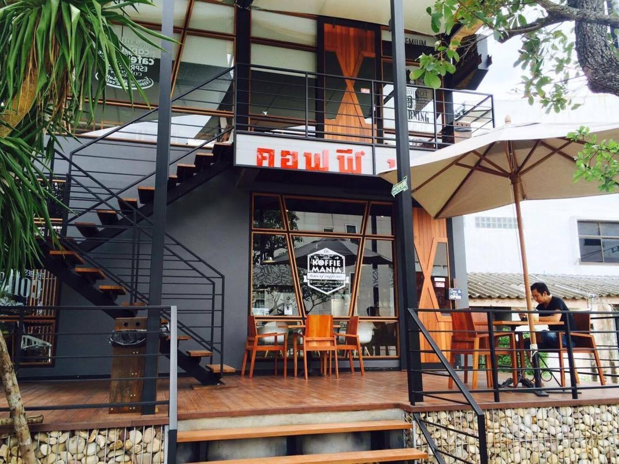 A modern building with a staircase leading to a second floor, a sign reading "NEW TO," and outdoor seating with tables and chairs.