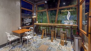 A cozy coffee shop interior with a wooden table, white chairs, and a patterned floor. - Loftmania Boutique Hotel (Chumphon)