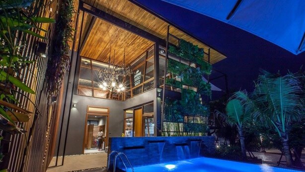 A modern building with a glass facade, a pool, and lush greenery. - Loftmania Boutique Hotel (Chumphon)