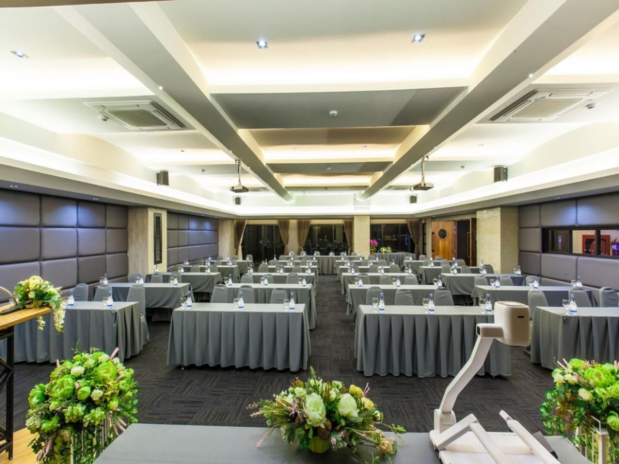 A conference room with multiple tables, grey tablecloths, and floral centerpieces.