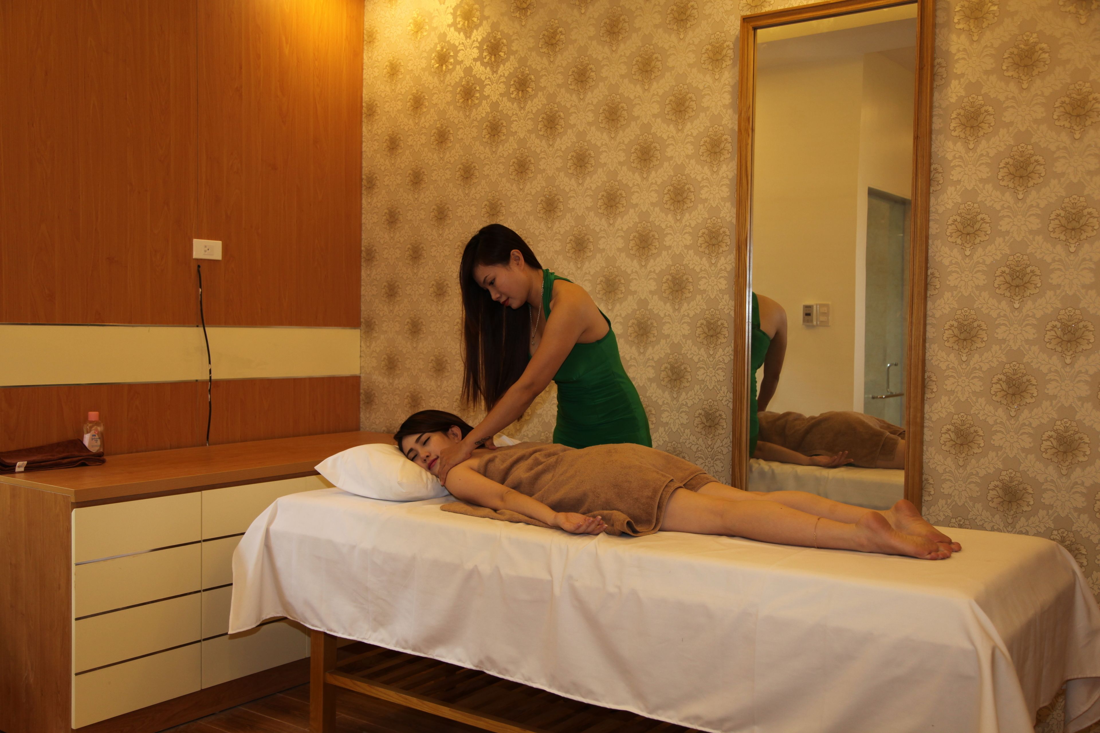 A massage therapy room with a wooden panel wall, a large mirror, and a massage table.