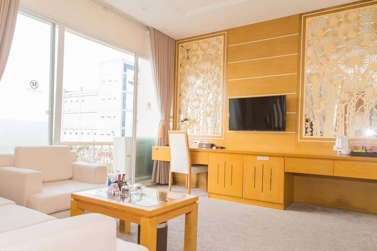 Een hotelkamer met een bank, een salontafel, een bureau met stoel, een televisie en een decoratief paneel.