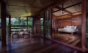 Una cabaña de madera con una cama grande, un escritorio y una silla. Cuenta con un balcón con barandilla y una planta.