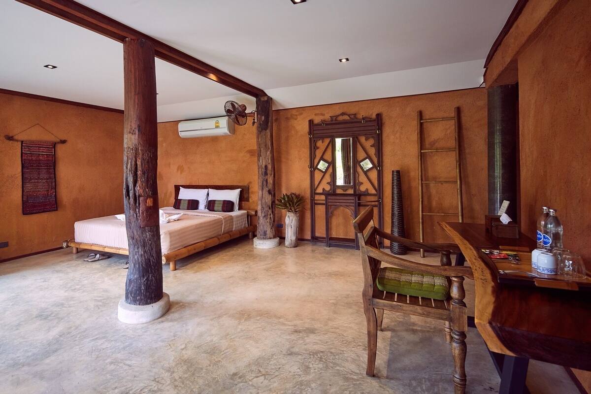 A bedroom with a bed, wooden furniture, a fan, and a wooden door.