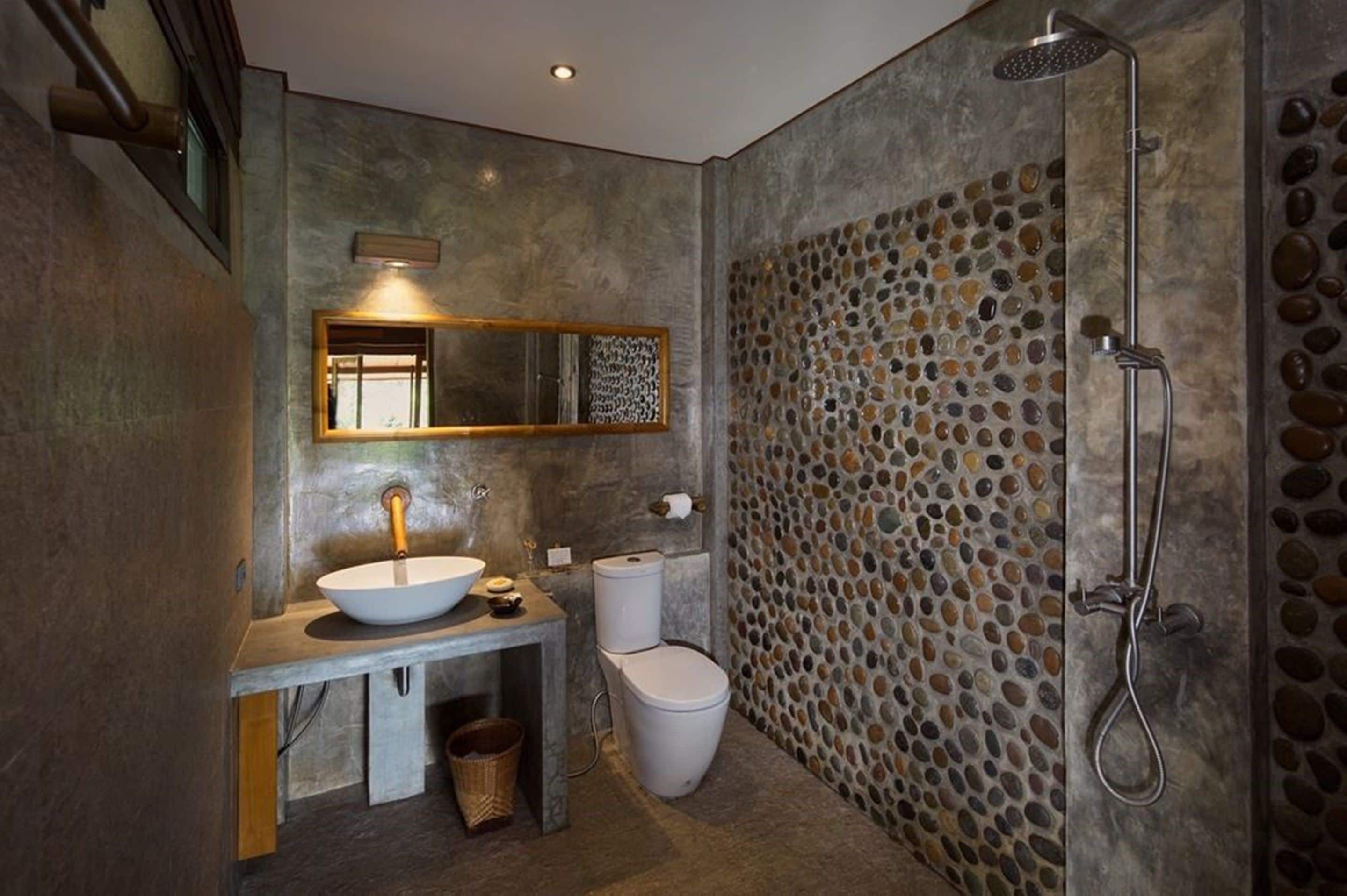 A bathroom with a stone wall, a sink, a toilet, and a shower.