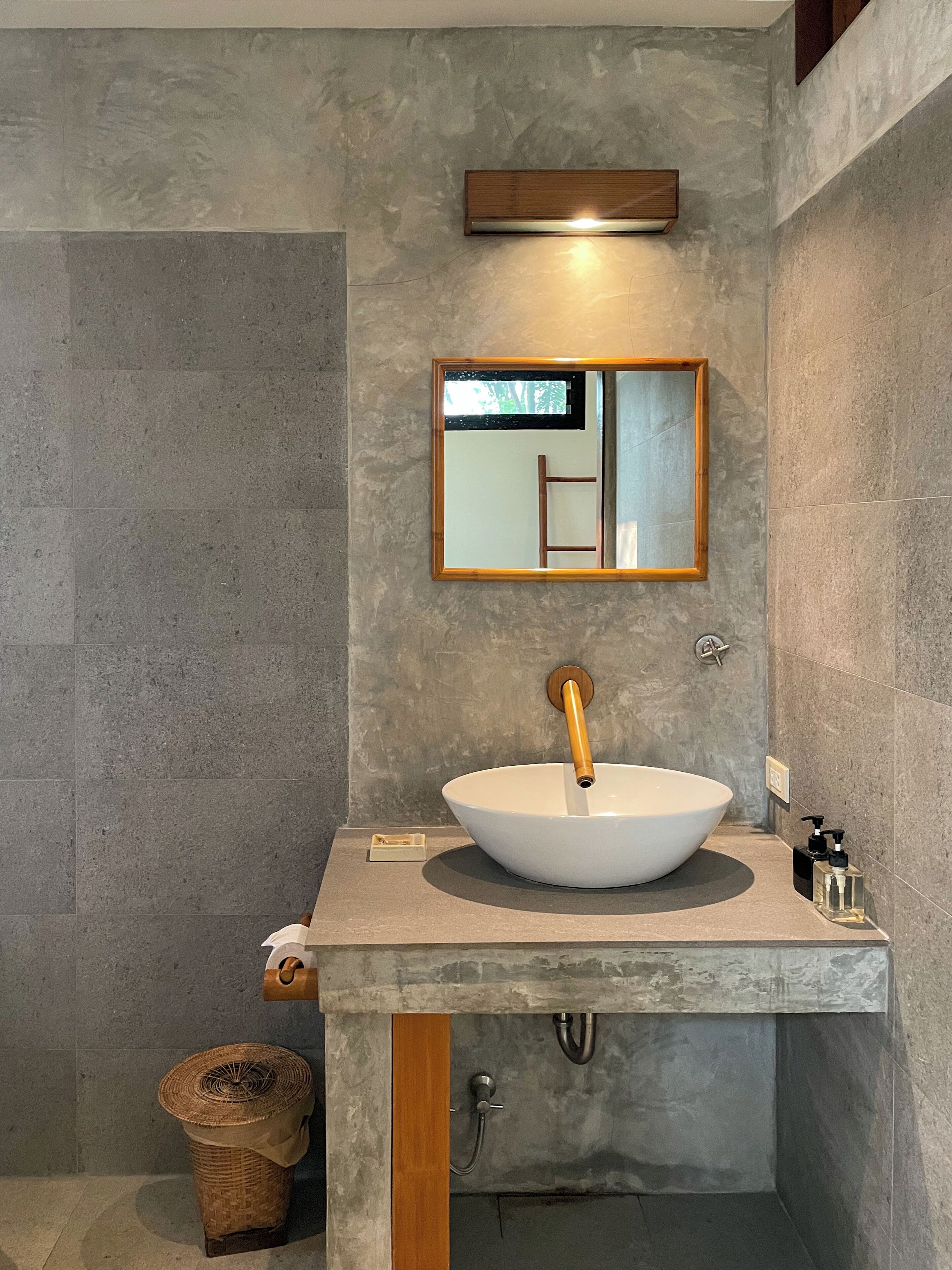 A modern bathroom with a large vessel sink, a wooden-framed mirror, and a textured wall.