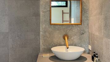 A modern bathroom with a large vessel sink, a wooden-framed mirror, and a textured wall.