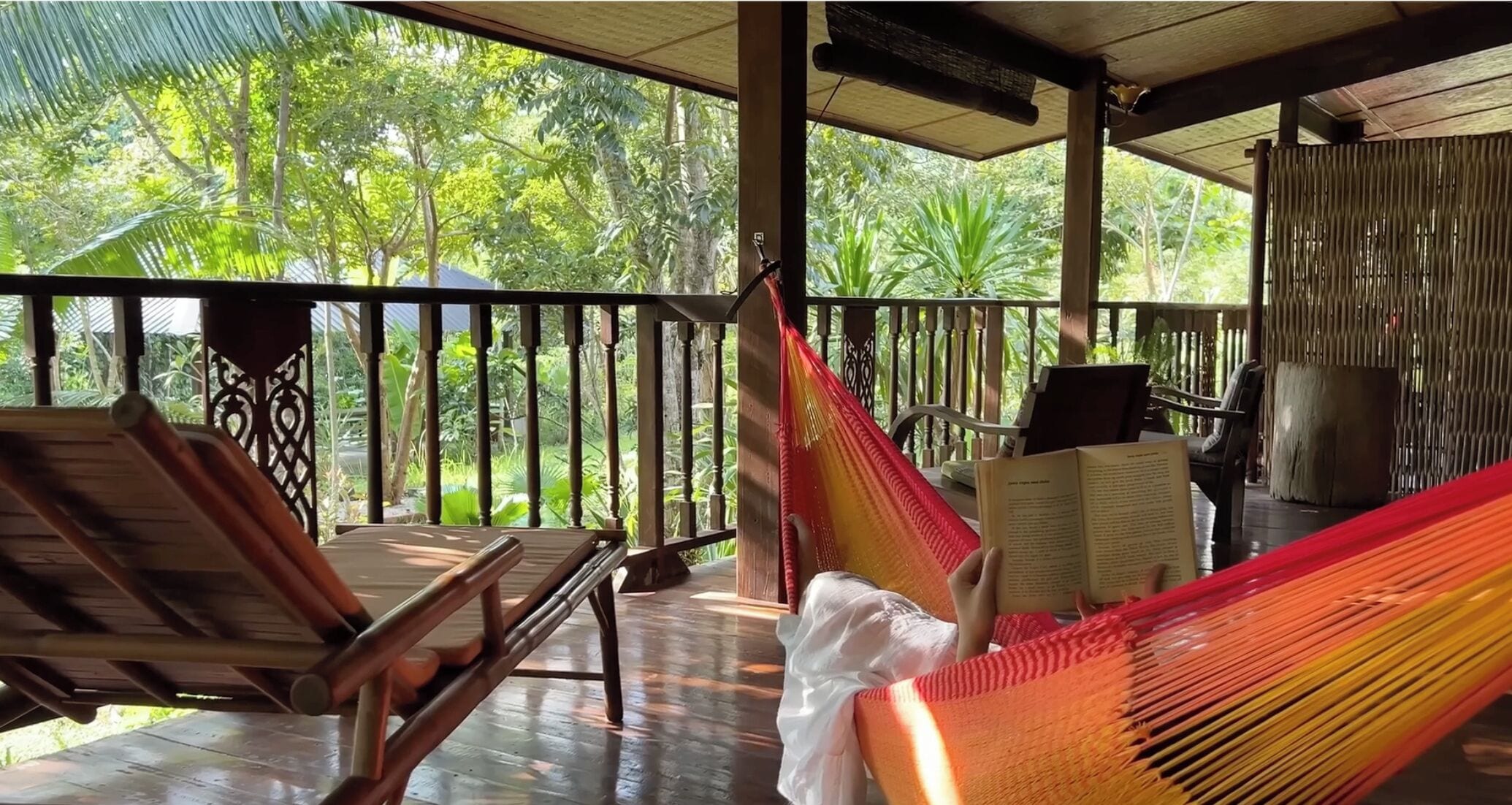 A hammock chair on a wooden deck with a view of lush greenery.