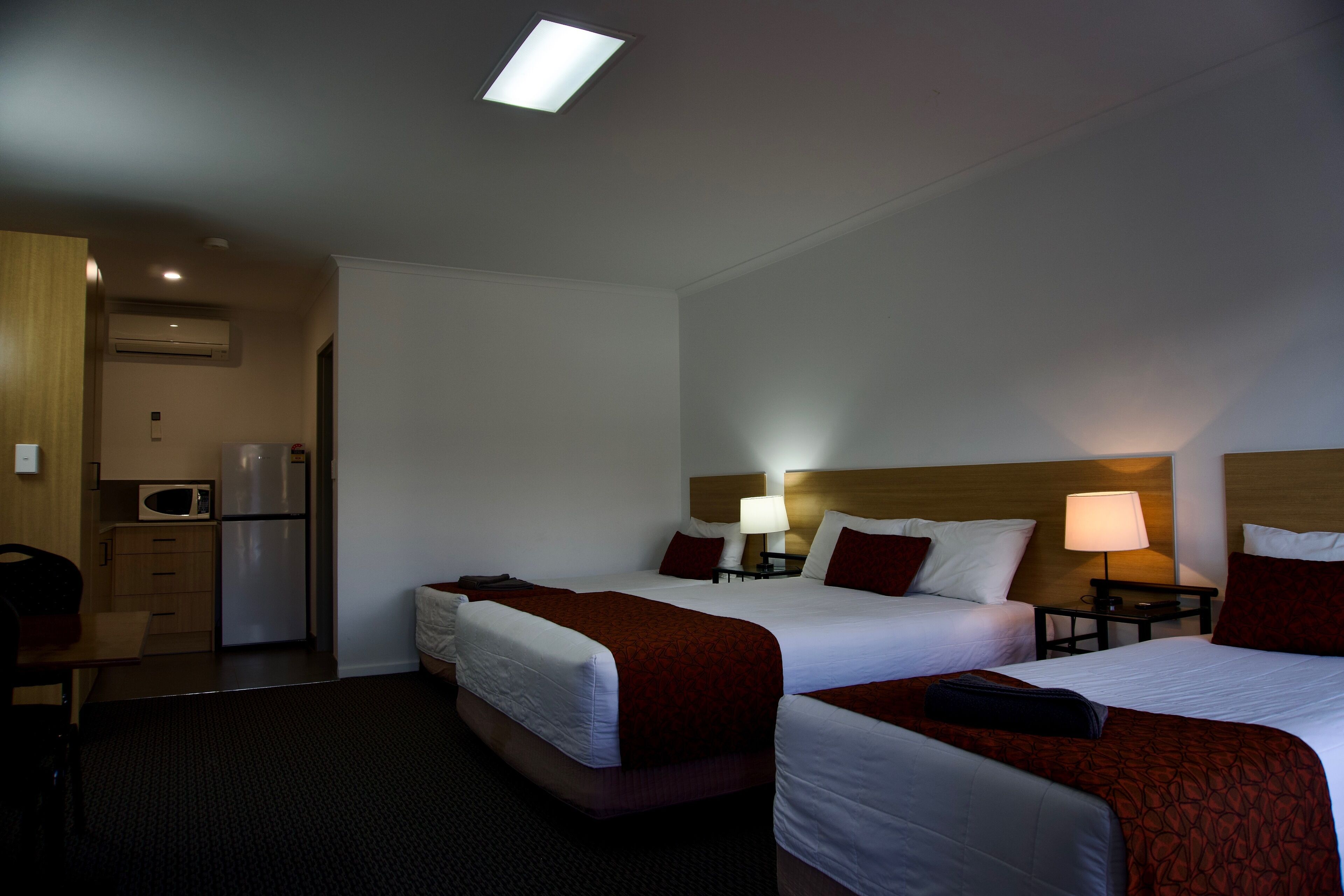 A hotel room with two beds, a kitchenette, and a ceiling light.