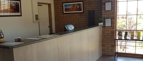 A reception area with a reception desk, a red welcome mat, and a window with a view of greenery.