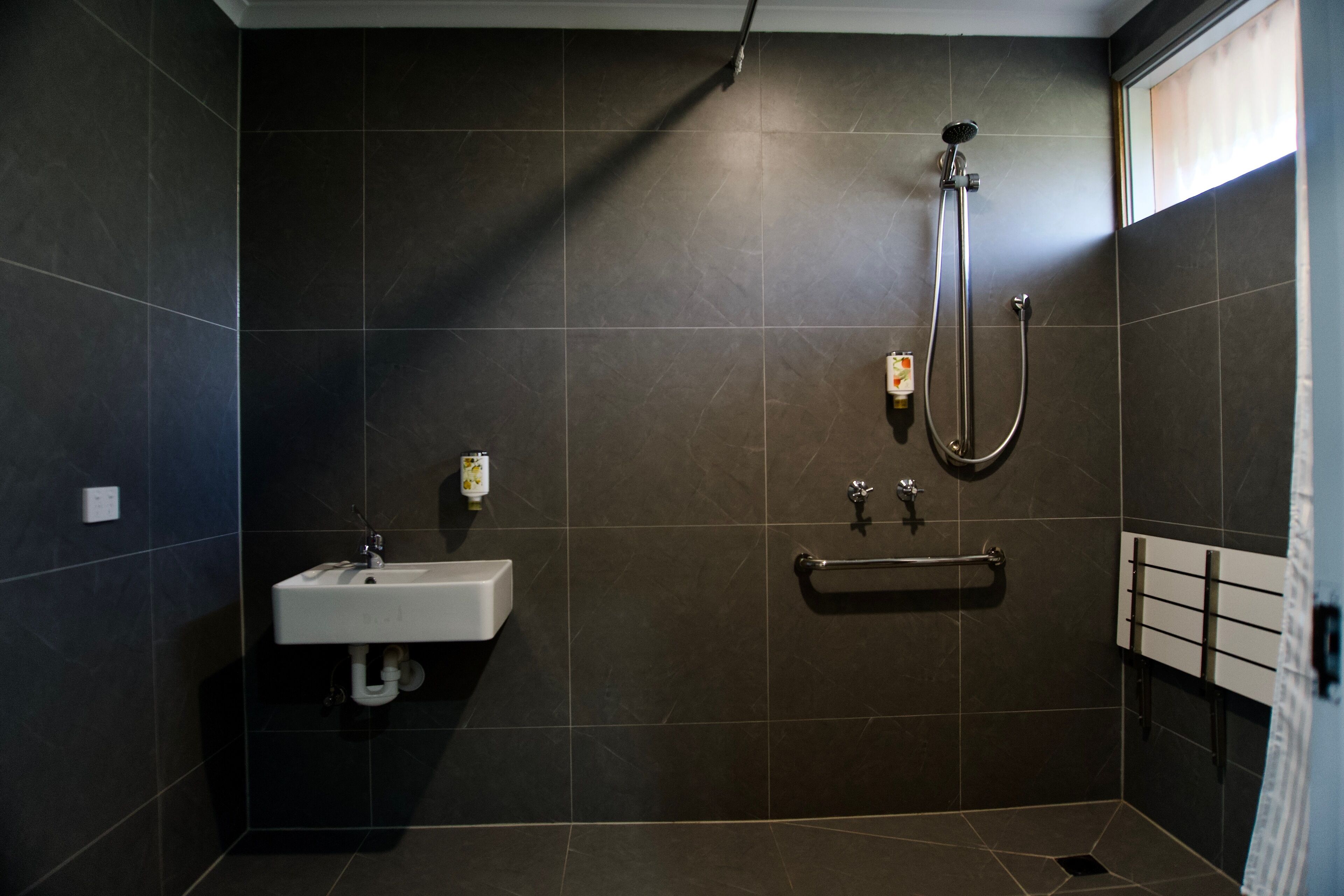 A bathroom with dark tiles, a white sink, a handheld showerhead, and a towel rack.