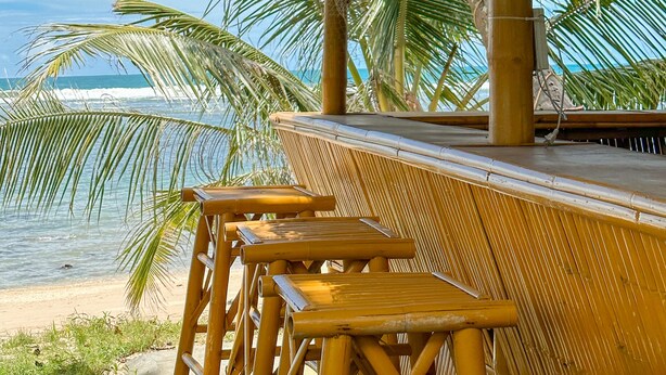 Ein Strandhaus mit einem Reetdach und Sitzgelegenheiten aus Bambus.