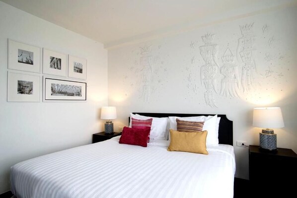 Habitación de hotel con una cama grande, varias almohadas, dos mesitas de noche con lámparas y cuadros en la pared.