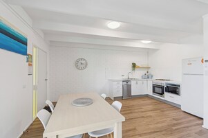 Una cocina moderna con armarios blancos, un reloj en la pared y un comedor con mesa y sillas.