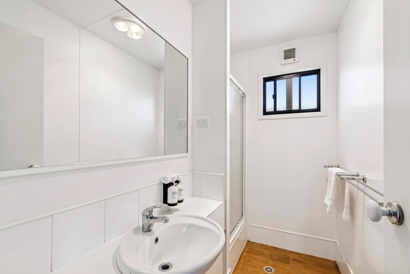 Un baño moderno con lavamanos, espejo y ducha blancos.